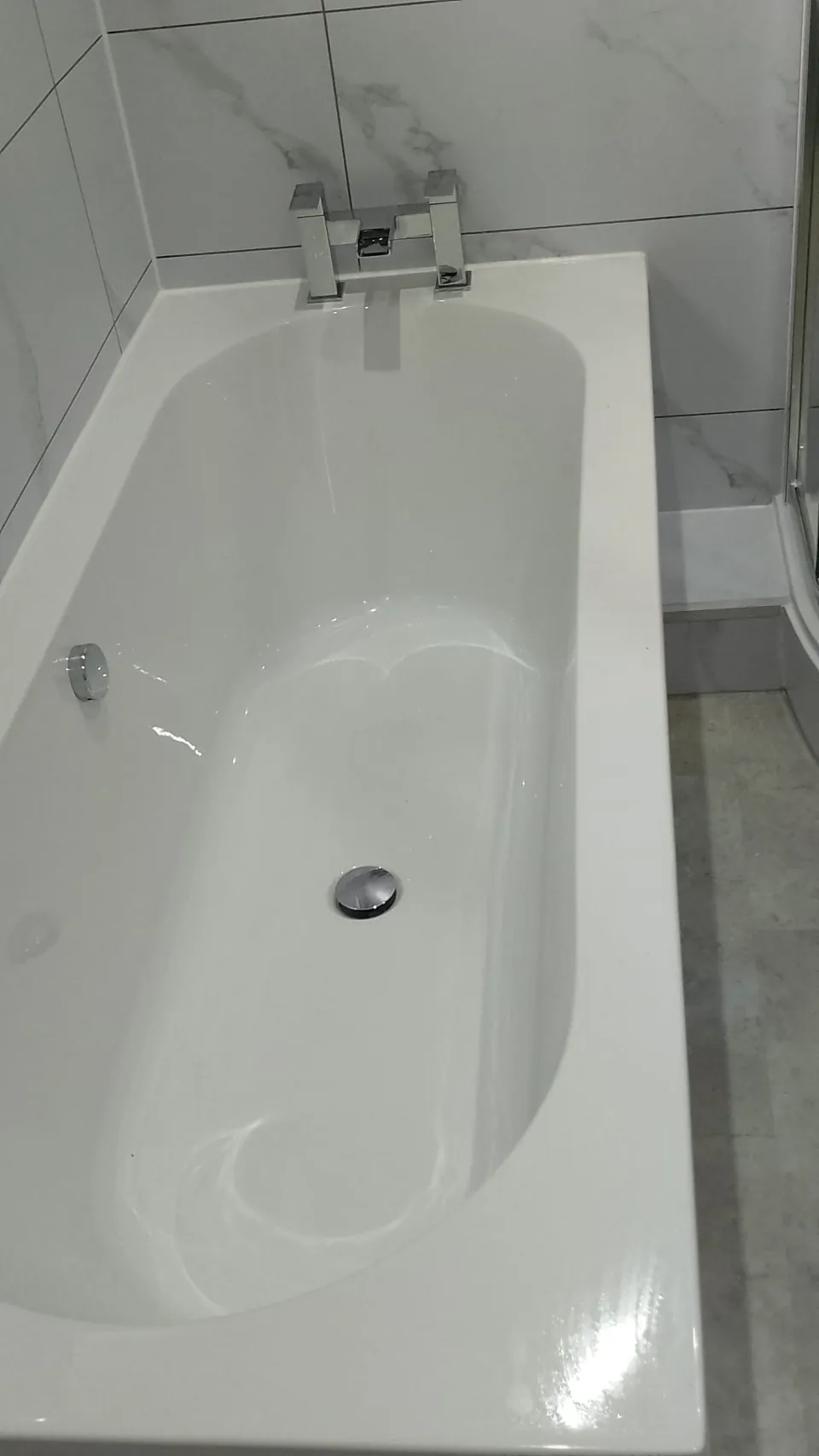 White fitted bath with marble-effect panel and walls